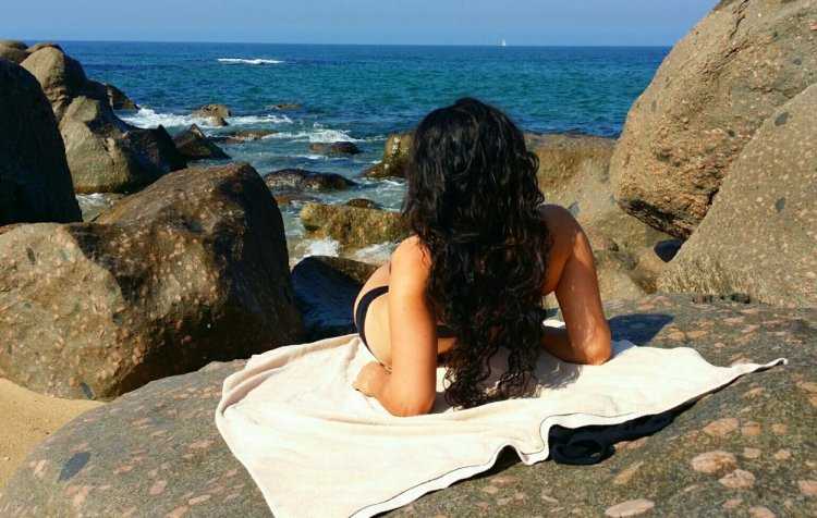 Искушенная кучерявая брюнетка спиной к морю