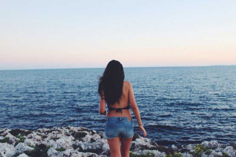 Соблазнительная брюнетка в шортах, спрятавшаяся ото всех на берегу моря