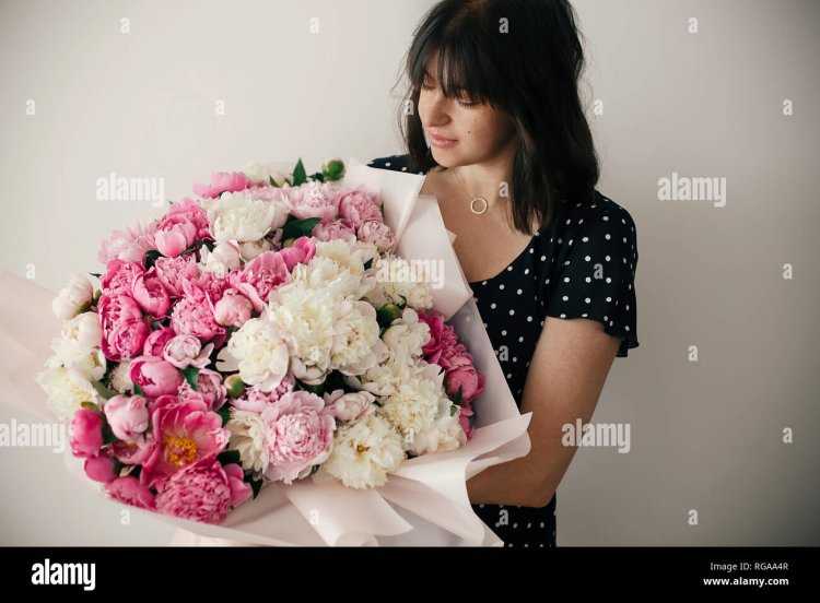 Девушка брюнетка со спины с белыми пионами в городе